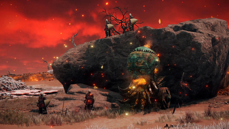 A large red rock, around which are clustered soldiers in red and gold uniforms, and a two-wheeled tank with a bronze humanoid face and a flamethrower mouth.