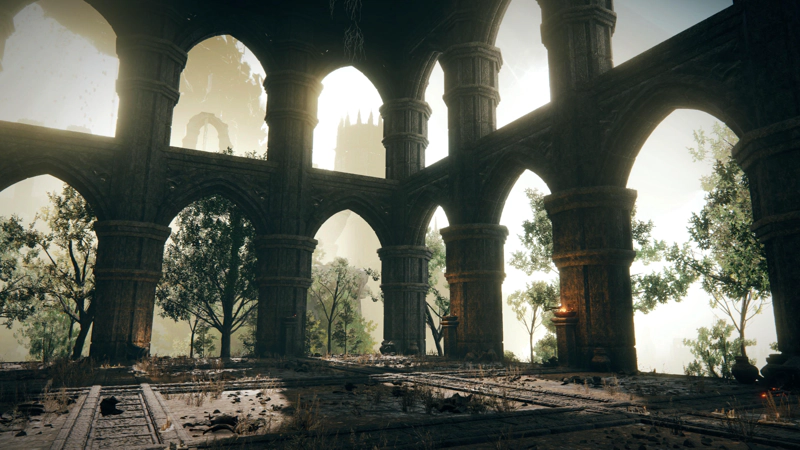 The interior of a two-storey stone structure built of octagonal columns and pointed arches. The paved floor is overgrown with yellow grasses and scattered with debris, but the braziers still burn with orange flame. Through the archways, green leafy trees stand against a misty pink backdrop of distant silhouettes.