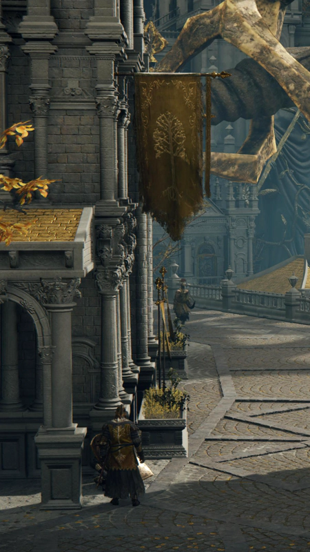 A view down a street in the Capital. A golden Erdtree banner drapes from a flagpole, and two gold-clad knights patrol the sun-dappled paving.