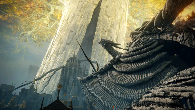 The vast fallen wing of a stone dragon, beneath the glorious golden trunk of the Erdtree. The dragon's head is raised towards the tree, and beyond, a tall domed structure rises to the highest point in the Capital, surrounded by vast tree roots.