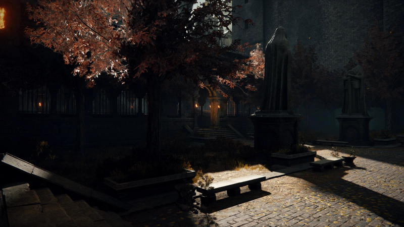 A paved courtyard at sunset. Golden light filters through red-grey foliage, while stone benches and statues of robed figures cast long shadows.