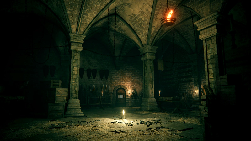 A grace in a large chamber, strewn with straw. Shields and weaponry are stacked against the walls, and a small wooden door with metal bars can be seen at the back of the room.
