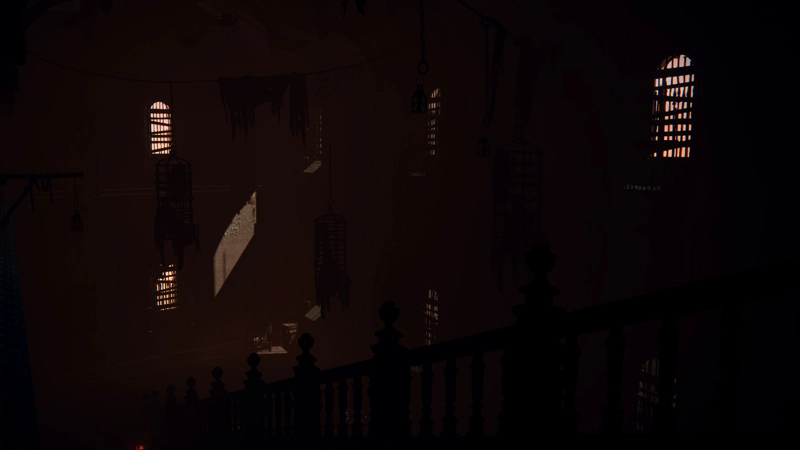 A dark room, with the balustrade of a set of stairs leading from mid-right to bottom-left. The silhouettes of iron cages dangle in the gloom, and only the most sparing snatches of light peek in through heavily barred windows.
