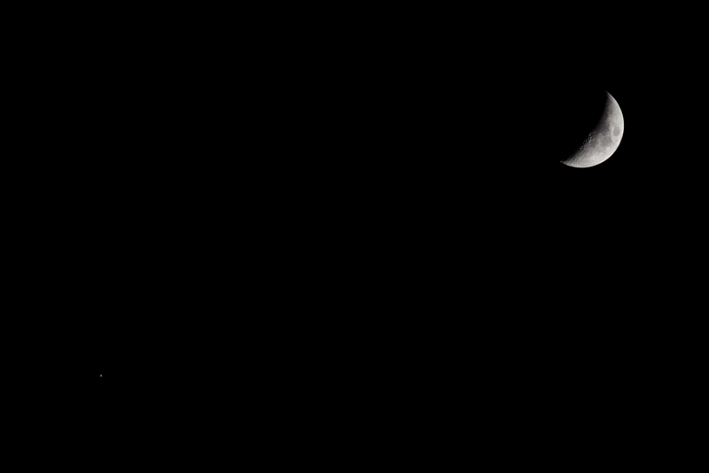 A wide shot of the night sky, with the crescent moon crisp and clear in the top-right corner, and a speck of light - Jupiter - in the bottom-left corner.