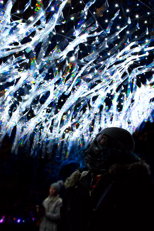 A woman in scarf and hat, looking up at a forest of diaphonous streamers dangling overhead.