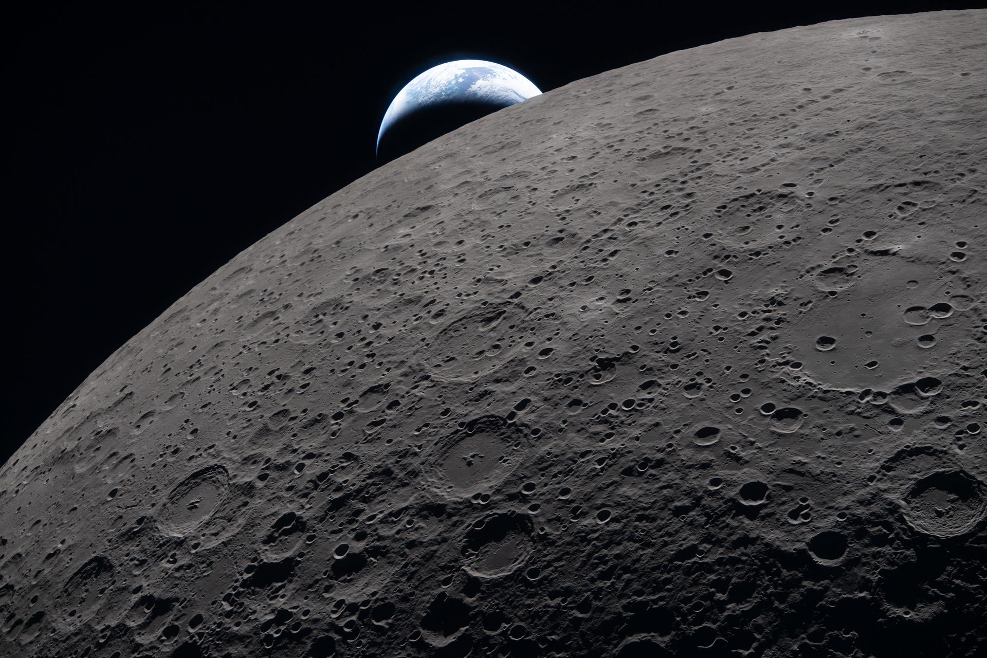 A close-up of the lunar surface from the Artemis II fly-by, with the white-and-blue sphere of Earth setting behind the Moon in the distance.